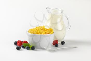 bowl of corn flakes and jug of milk on on off-white background with shadows