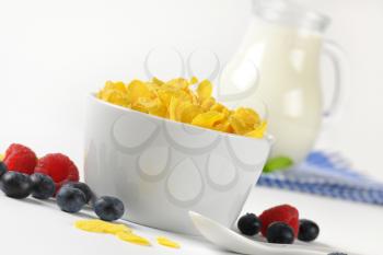 bowl of corn flakes and jug of milk on checkered dishtowel
