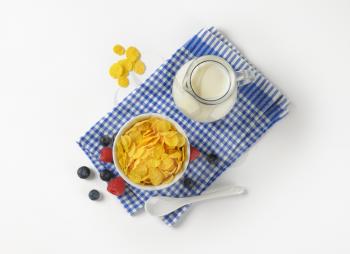 bowl of corn flakes and jug of milk on checkered dishtowel