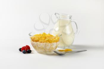 bowl of corn flakes and jug of milk on off-white background with shadows