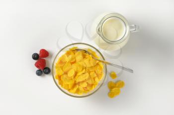 bowl of corn flakes and jug of milk on off-white background with shadows
