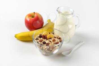 bowl of oat flakes with raisins, jug of milk, banana and apple