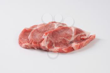 three raw pork neck chops on white background