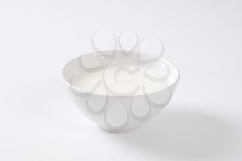 bowl of fresh milk on off-white background with shadows