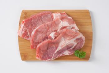 three raw pork neck chops  on wooden cutting board