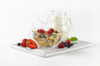 bowl of cereals and berry fruit with jug of milk on wooden cutting board