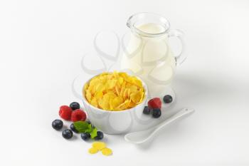bowl of corn flakes and jug of milk on white background