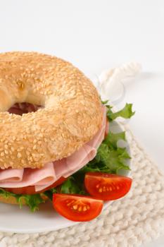 sesame bagel sandwich with ham on white plate