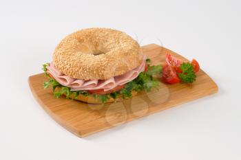 sesame bagel sandwich with ham on wooden cutting board