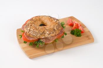 bagel sandwich with salami on wooden cutting board