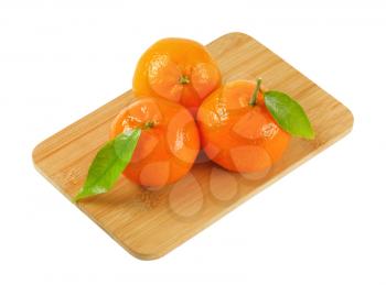 three tangerines with leaves on wooden cutting board