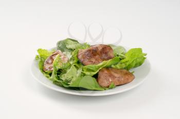 plate of pan fried liver with greens on white background