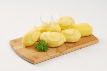 heap of peeled potatoes on wooden cutting board