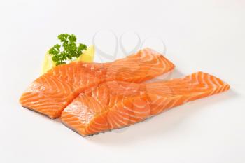 raw salmon fillets with lemon and parsley on white background
