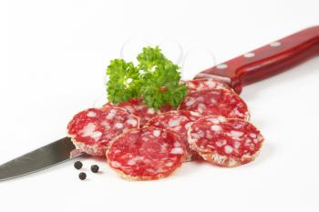thin slices of dry cured sausage and kitchen knife on white background