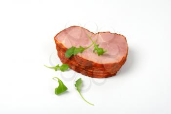 stack of sliced smoked pork meat with arugula leaves on white background