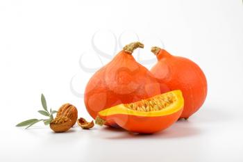 orange pumpkins with walnuts and sprig of sage on white background