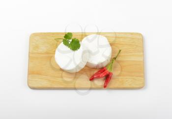 Wheels of soft white cheese and red chili peppers on cutting board