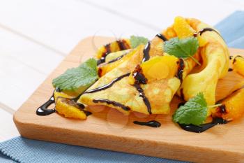 crepes with oranges and chocolate syrup on wooden cutting board