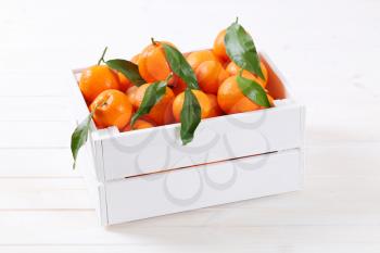 box of fresh tangerines with leaves on white background