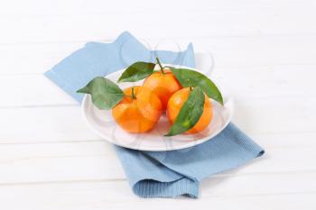 plate of fresh tangerines with leaves on blue place mat
