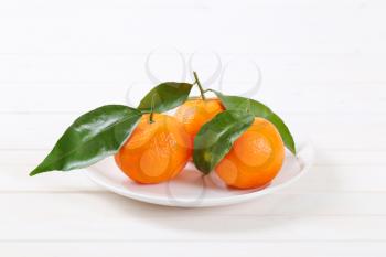 plate of fresh tangerines with leaves on white background