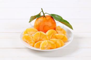 whole and peeled tangerines on white plate