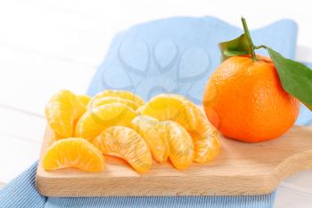whole and peeled tangerines on wooden cutting board - close up