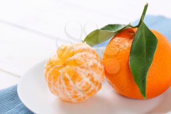 whole and peeled tangerines on white plate - close up