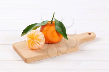 whole and peeled tangerines on wooden cutting board