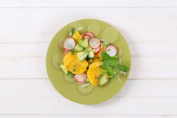 plate of radish and cucumber salad with orange slices on white background