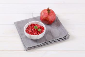 ripe pomegranate with bowl of seeds on grey place mat