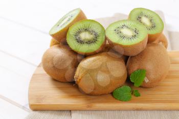 pile of whole and halved kiwi fruits on wooden cutting board