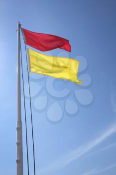 red and yellow safe bathing area flag against blue sky