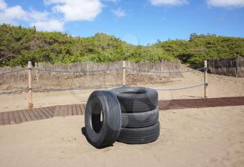 Four used tires abandoned next to wooden walkway on sandy beach