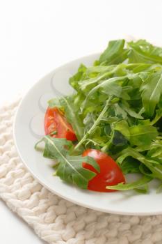 plate of arugula and tomato salad on white table mat