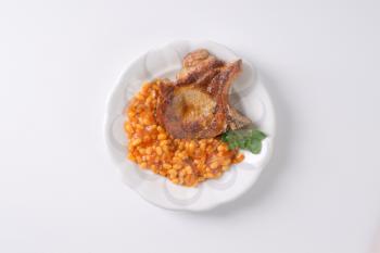 roasted pork chop and baked beans in tomato sauce on white plate