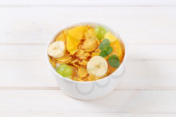 bowl of corn flakes with milk and fresh fruit on white background