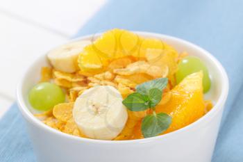 bowl of corn flakes with milk and fresh fruit on blue place mat - close up