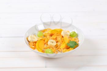 plate of corn flakes with milk and fresh fruit on white background