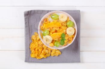 bowl of corn flakes with milk and fresh fruit on grey place mat
