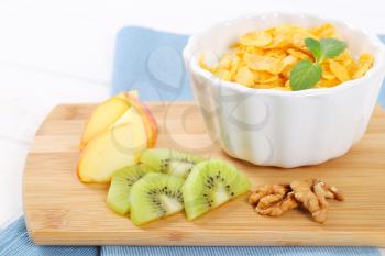 bowl of corn flakes with milk and fresh fruit on wooden cutting board - close up