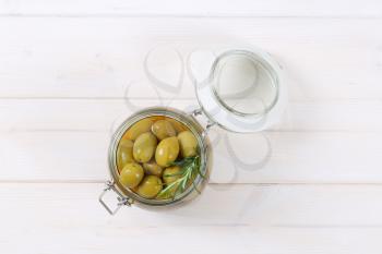 jar of green olives with fresh rosemary on white background