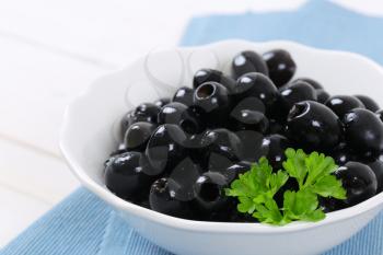 bowl of black olives with fresh parsley on blue place mat - close up