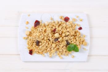 pile of morning granola with hazelnuts, raisins and cranberries on white cutting board