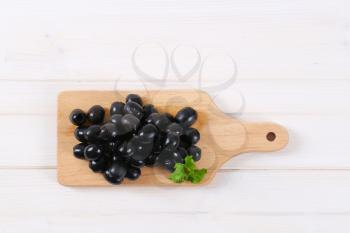 pile of black olives with fresh parsley on wooden cutting board