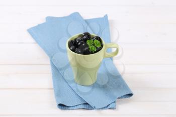 cup of black olives with fresh parsley on blue place mat