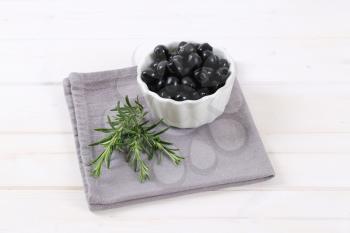 bowl of black olives with fresh rosemary on grey place mat