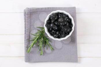 bowl of black olives with fresh rosemary on grey place mat