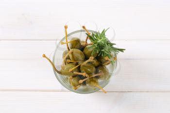 glass of pickled caper berries on white wooden background